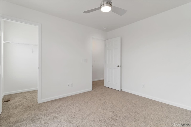 unfurnished bedroom with light carpet, a spacious closet, a closet, and ceiling fan