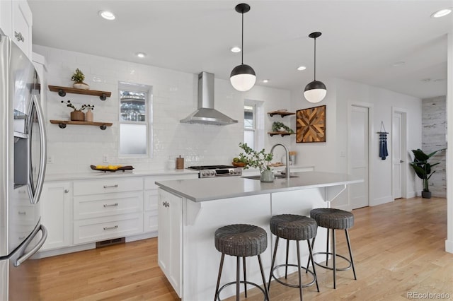 kitchen with wall chimney exhaust hood, sink, stainless steel fridge with ice dispenser, an island with sink, and white cabinets