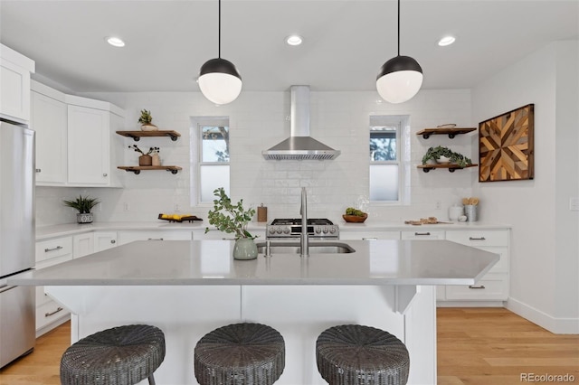 kitchen with a center island with sink, a breakfast bar, wall chimney exhaust hood, and appliances with stainless steel finishes