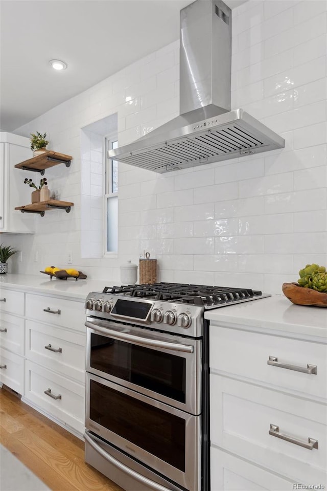 kitchen featuring white cabinetry, range with two ovens, tasteful backsplash, wall chimney exhaust hood, and light wood-type flooring