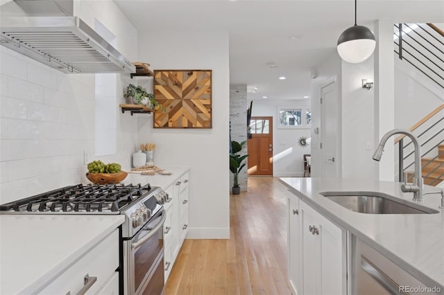 kitchen featuring pendant lighting, white cabinetry, sink, double oven range, and wall chimney range hood