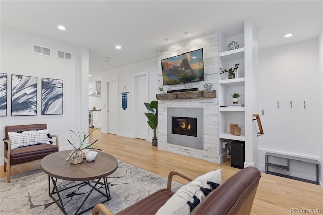 living room with built in shelves, a fireplace, and light wood-type flooring