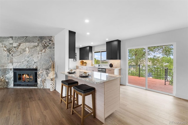 kitchen featuring light hardwood / wood-style floors, stainless steel dishwasher, a fireplace, and light stone countertops