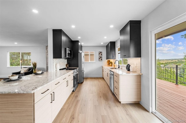 kitchen with light hardwood / wood-style floors, light stone countertops, stainless steel appliances, and tasteful backsplash