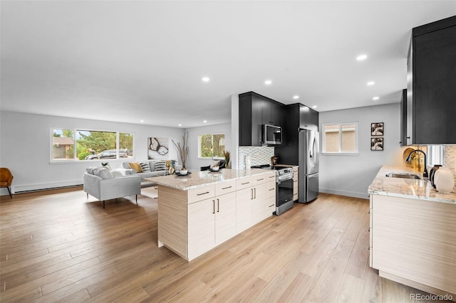 kitchen with light stone counters, appliances with stainless steel finishes, light wood-type flooring, and sink