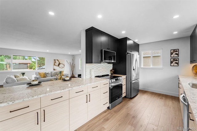 kitchen with light stone counters, tasteful backsplash, stainless steel appliances, light brown cabinetry, and light hardwood / wood-style floors