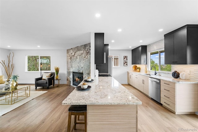 kitchen featuring stainless steel dishwasher, a fireplace, light stone countertops, and plenty of natural light