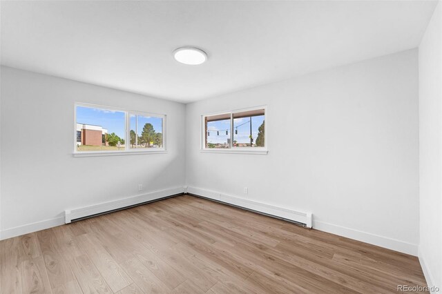 spare room featuring baseboard heating and light hardwood / wood-style flooring