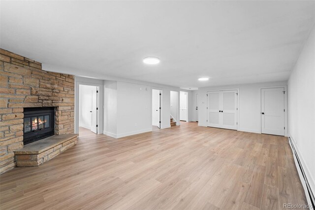 unfurnished living room featuring a stone fireplace, baseboard heating, and light hardwood / wood-style flooring