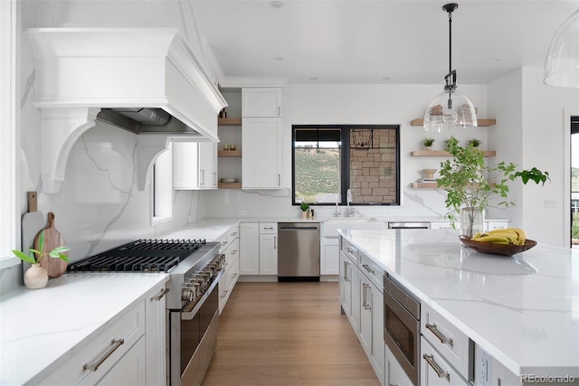 kitchen with light stone counters, hanging light fixtures, white cabinetry, light hardwood / wood-style flooring, and appliances with stainless steel finishes