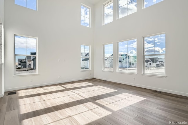 empty room featuring plenty of natural light, a towering ceiling, and light hardwood / wood-style flooring