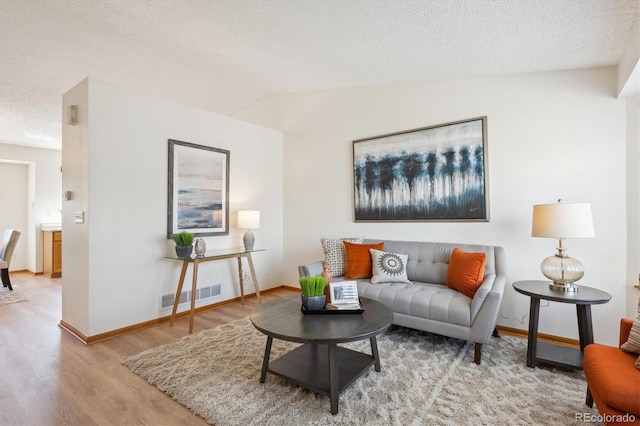 living area with visible vents, baseboards, wood finished floors, and vaulted ceiling