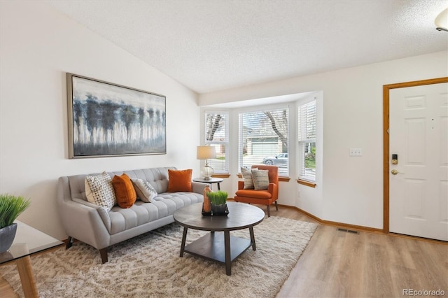 living area featuring light wood finished floors, a textured ceiling, baseboards, vaulted ceiling, and visible vents