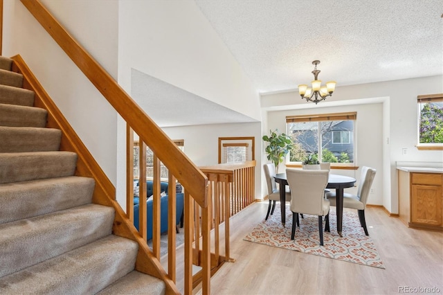 dining area featuring stairs, baseboards, a textured ceiling, light wood-style flooring, and a notable chandelier