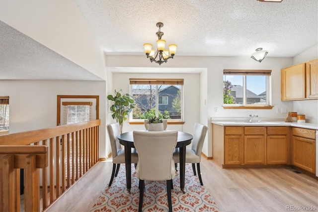 dining area featuring light wood-style floors, a healthy amount of sunlight, a textured ceiling, and a chandelier