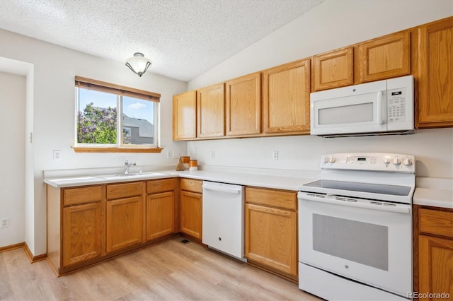 kitchen with a textured ceiling, a sink, light countertops, white appliances, and light wood-style flooring