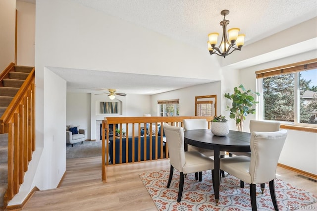 dining area featuring a textured ceiling, ceiling fan with notable chandelier, light wood-type flooring, visible vents, and stairway