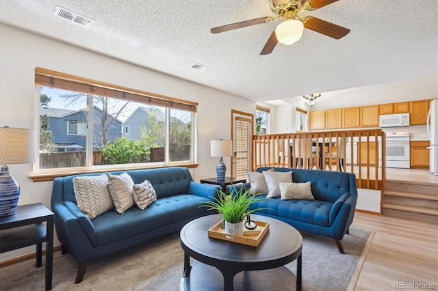 living area with visible vents, a ceiling fan, a textured ceiling, and light wood-type flooring