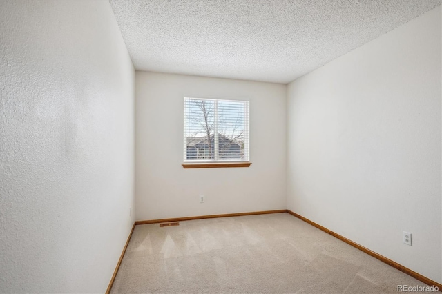 empty room with carpet floors, a textured ceiling, baseboards, and visible vents