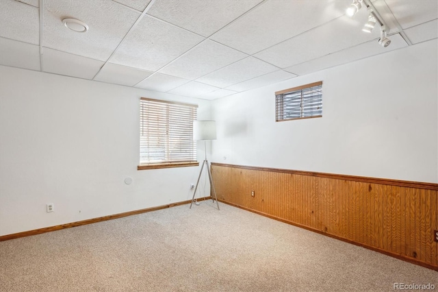 unfurnished room with wooden walls, a wainscoted wall, light carpet, and a paneled ceiling