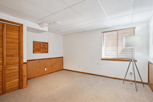 unfurnished bedroom with carpet, a drop ceiling, wainscoting, and wooden walls