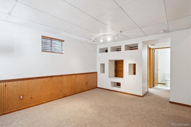 empty room featuring carpet flooring, wainscoting, rail lighting, wood walls, and built in shelves