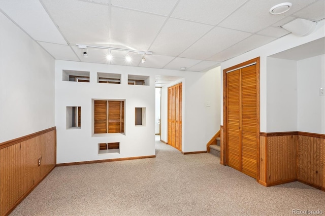 carpeted spare room with wooden walls, wainscoting, stairs, and a paneled ceiling