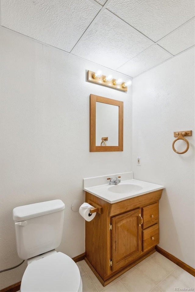 half bath with baseboards, tile patterned flooring, toilet, and vanity