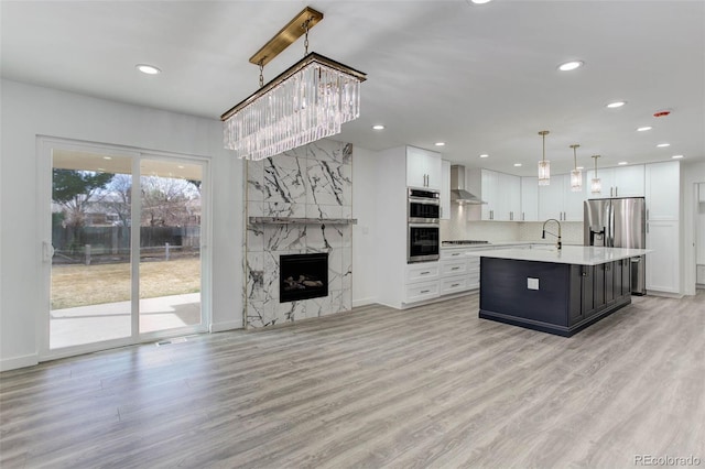 kitchen featuring a sink, stainless steel appliances, light countertops, wall chimney exhaust hood, and light wood-type flooring