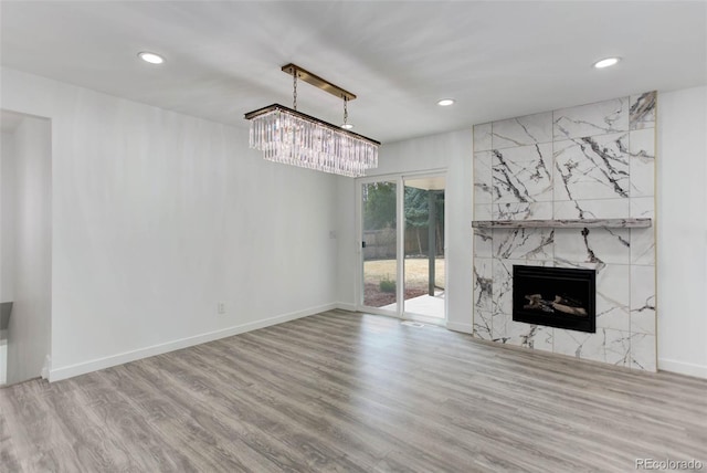 unfurnished living room with a chandelier, recessed lighting, a high end fireplace, and wood finished floors