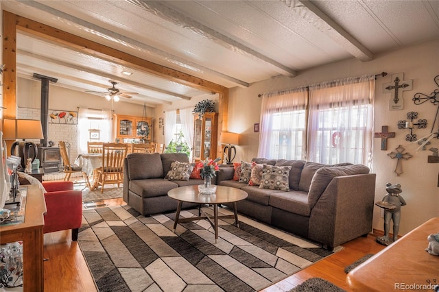 living room featuring plenty of natural light, beam ceiling, wood-type flooring, and a wood stove