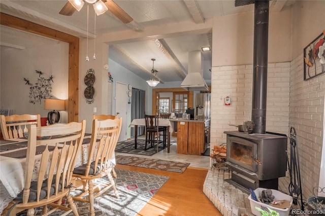 dining room featuring brick wall, lofted ceiling with beams, a wood stove, ceiling fan, and light wood-type flooring