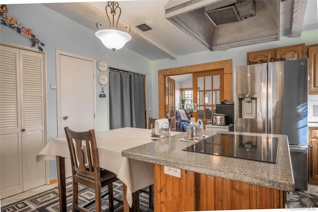 kitchen with light stone counters, black electric stovetop, lofted ceiling with beams, decorative light fixtures, and custom exhaust hood