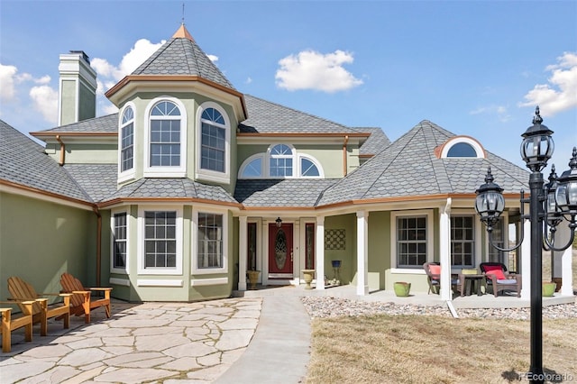 view of front of home with a high end roof, stucco siding, a chimney, and a patio