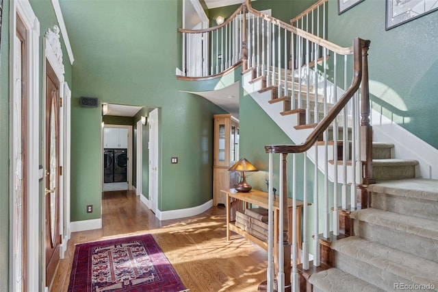 interior space featuring baseboards, wood finished floors, a towering ceiling, and washer and clothes dryer