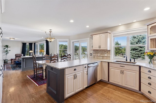 kitchen with light wood finished floors, decorative backsplash, dishwasher, and a sink