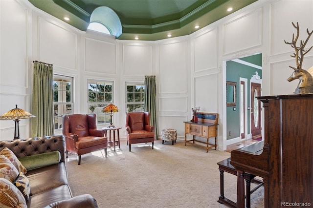 sitting room with a decorative wall, ornamental molding, a high ceiling, and light carpet