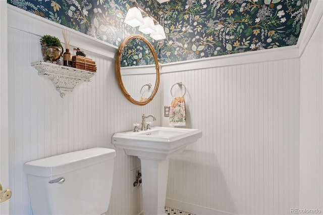 bathroom with a wainscoted wall, toilet, wallpapered walls, and a sink