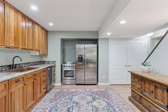 kitchen with light wood finished floors, recessed lighting, a sink, stainless steel appliances, and brown cabinets