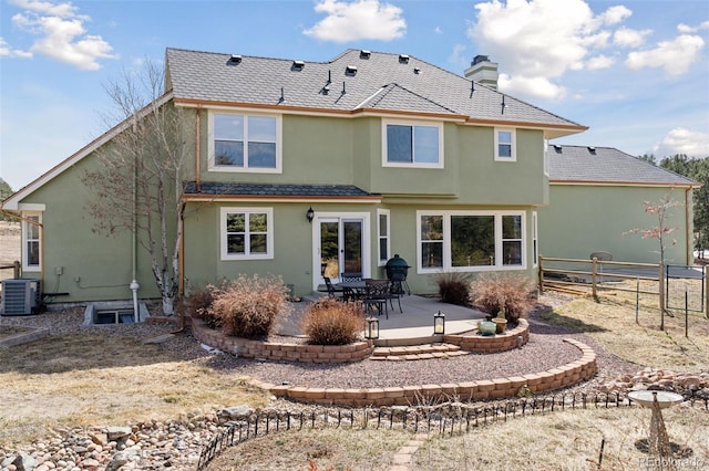 rear view of property featuring fence, stucco siding, central AC unit, a chimney, and a patio area