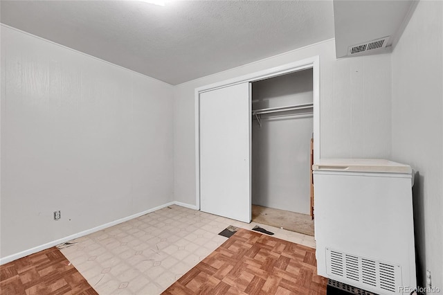 unfurnished bedroom with a textured ceiling, refrigerator, light parquet floors, and a closet