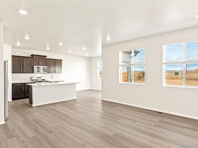 kitchen with light hardwood / wood-style floors, an island with sink, appliances with stainless steel finishes, a wealth of natural light, and dark brown cabinetry