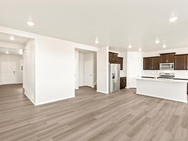 kitchen with light wood-type flooring, stainless steel appliances, backsplash, and an island with sink