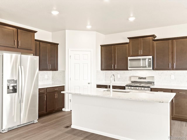 kitchen featuring light stone countertops, stainless steel appliances, tasteful backsplash, an island with sink, and sink