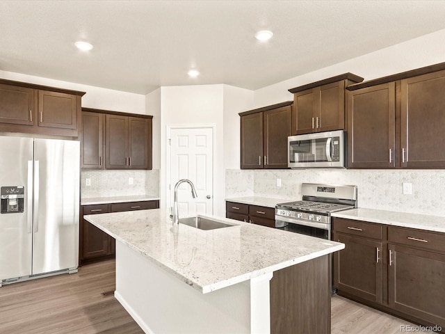 kitchen with light stone countertops, stainless steel appliances, a center island with sink, and sink