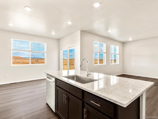 kitchen featuring a kitchen island with sink, stainless steel dishwasher, light stone counters, and sink