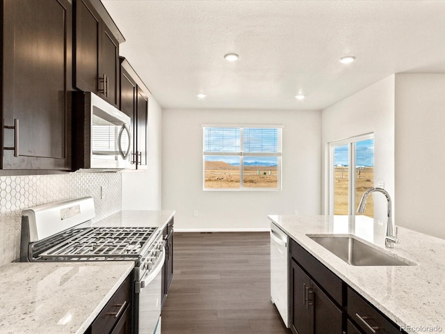 kitchen with appliances with stainless steel finishes, tasteful backsplash, dark brown cabinets, light stone countertops, and sink