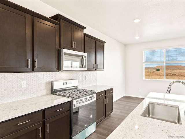 kitchen with appliances with stainless steel finishes, dark wood-type flooring, light stone counters, dark brown cabinetry, and sink