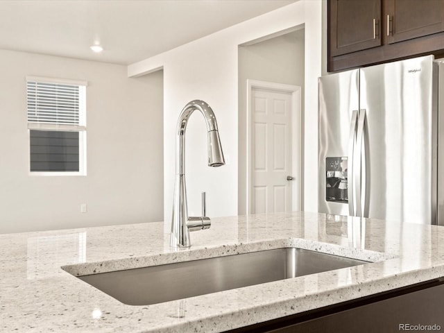 kitchen with stainless steel refrigerator with ice dispenser, light stone countertops, sink, and dark brown cabinetry