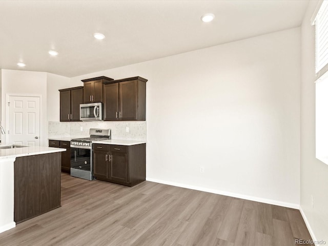 kitchen with dark brown cabinetry, stainless steel appliances, decorative backsplash, sink, and light hardwood / wood-style floors